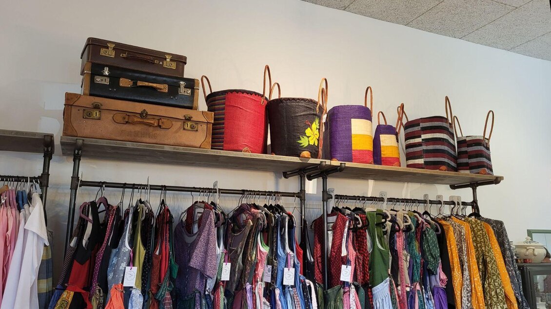 Ein Regal mit bunten Körben und alten Koffern. Darunter hängen verschiedene Kleidungsstücke in verschiedenen Farben. | © Petra Kirchschlager