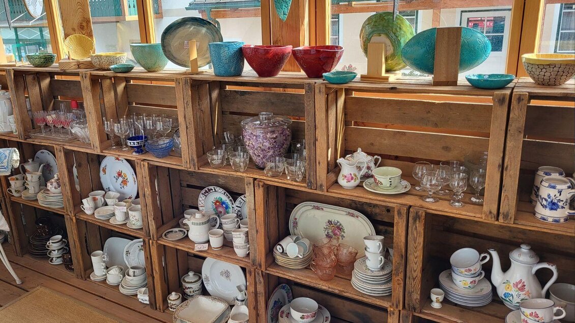 Eine Mauer aus Holzkisten, gefüllt mit Geschirr und Glaswaren. Die Regale zeigen eine Vielfalt von farbenfrohen Tellern, Tassen und Gläsern. | © Petra Kirchschlager