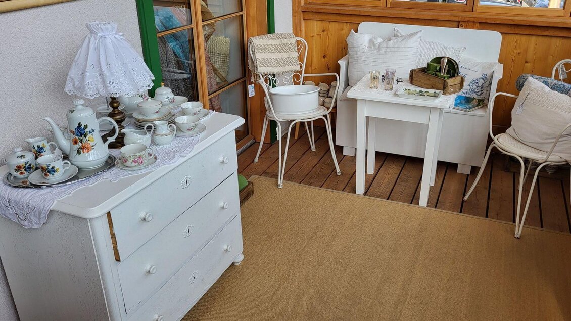 Ein gemütlicher Raum mit weißen Möbeln und einer Tischecke. Auf der Kommode stehen feine Teegeschirre und Dekorationen. | © Petra Kirchschlager