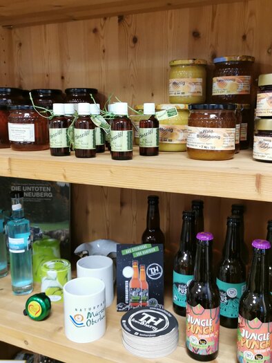A shelf with various foods and drinks. There are jams, beverages, and bottles in different sizes.