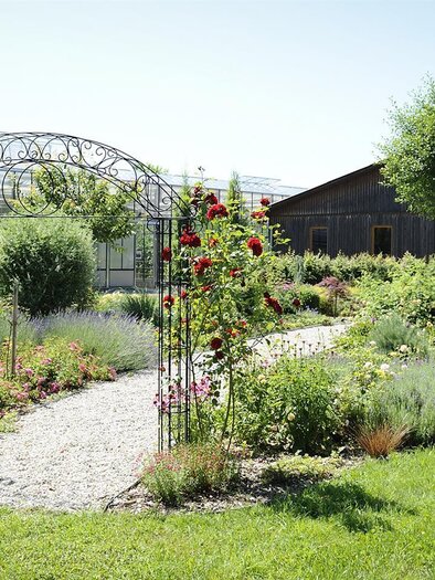 A beautiful garden with colorful flowers and well-designed paths. In the background, greenhouses and a wooden building can be seen. | © Versuchsstation für Spezialkulturen
