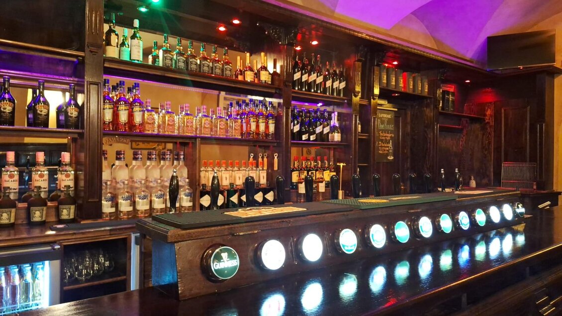 Eine gut gefüllte Bar mit einer Auswahl an Spirituosen und bunten Lichtern. Der Holzregal bietet eine einladende Atmosphäre. | © Victor Muntean