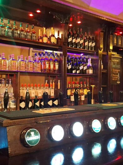 A well-stocked bar with a selection of spirits and colorful lights. The wooden shelf provides an inviting atmosphere. | © Victor Muntean