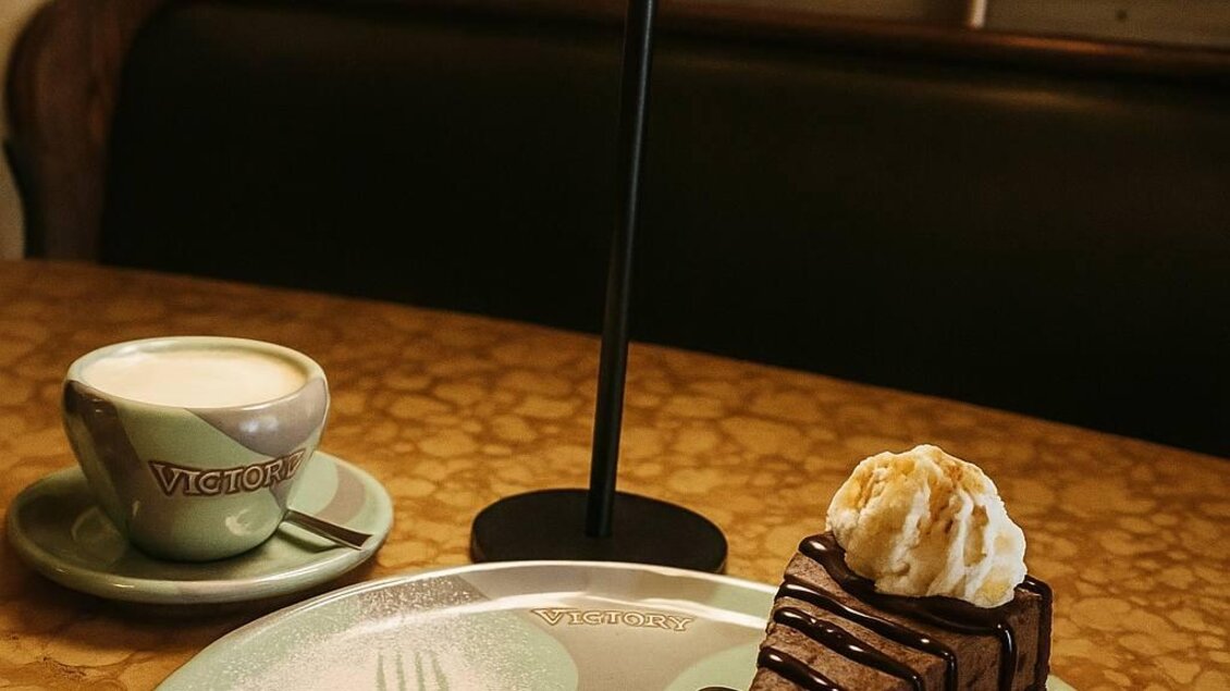 Eine Tasse Kaffee steht neben einem Stück Schokoladentorte auf einem Teller. Die Torte ist mit Schokolade und einer Kugel Eis dekoriert. | © Victor Muntean