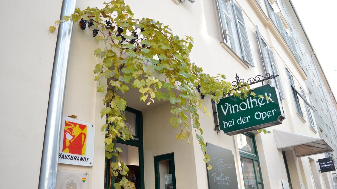 Ein Weinlokal mit dem Namen "Vinothek bei der Oper", umgeben von einer Rebenbewachsung. Die Fassade ist hell und freundlich gestaltet. | © Vinothek bei der Oper