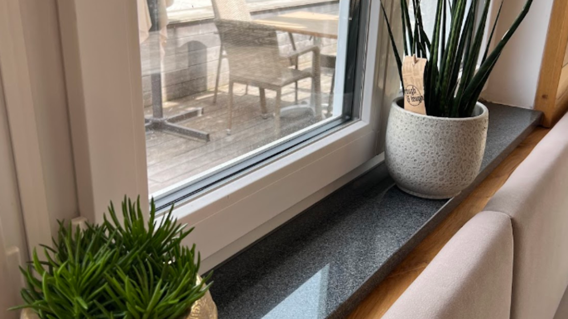 Zwei Pflanzentöpfe stehen auf der Fensterbank, einer in Form eines Gesichts und der andere rund und schlicht. Im Hintergrund sind Stühle und Tische auf einer Terrasse sichtbar. | © Vivo Pizzeria