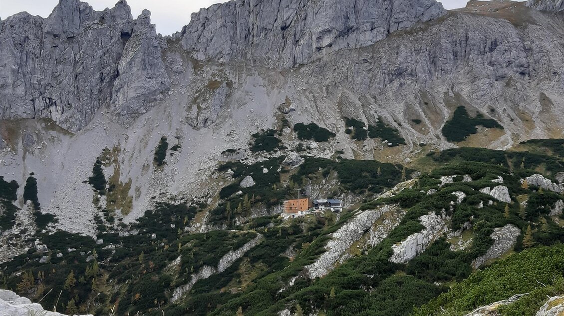 Eine beeindruckende Berglandschaft mit steilen Felsen und grünen Hügeln. Im Hintergrund ist ein kleines Gebäude zu sehen.