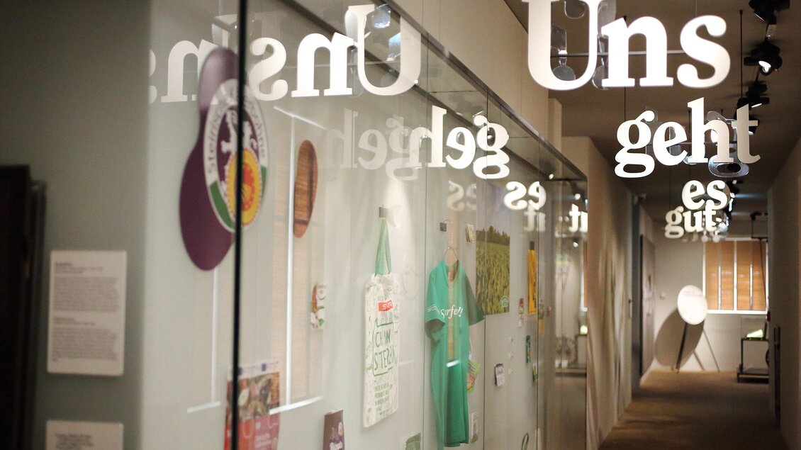 Ein modernes Ausstellungsumfeld mit Glaswänden und verschiedenen Kunstwerken. Sichtbare Texte und Objekte bieten einen Einblick in die Ausstellung. | © Universalmuseum Joanneum - J. Kucek +