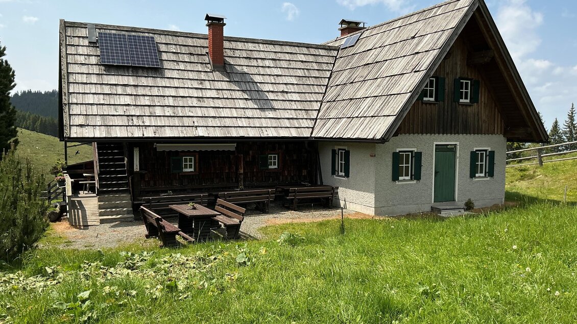 Eine traditionelle Berghütte umgeben von Wiesen und Bäumen. Das Dach ist mit Solarzellen ausgestattet und das Wetter ist klar. | © Margareta Köstner