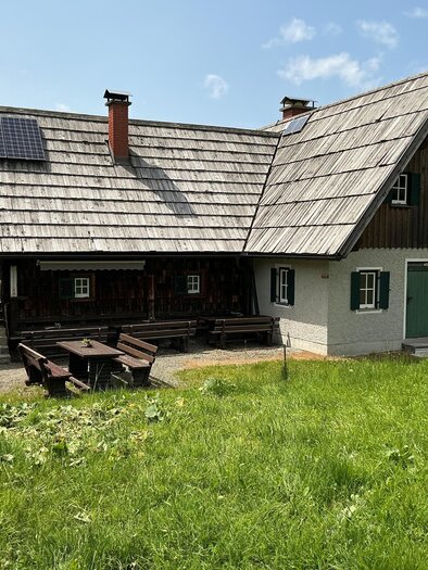 A traditional mountain hut surrounded by meadows and trees. The roof is equipped with solar panels and the weather is clear. | © Margareta Köstner