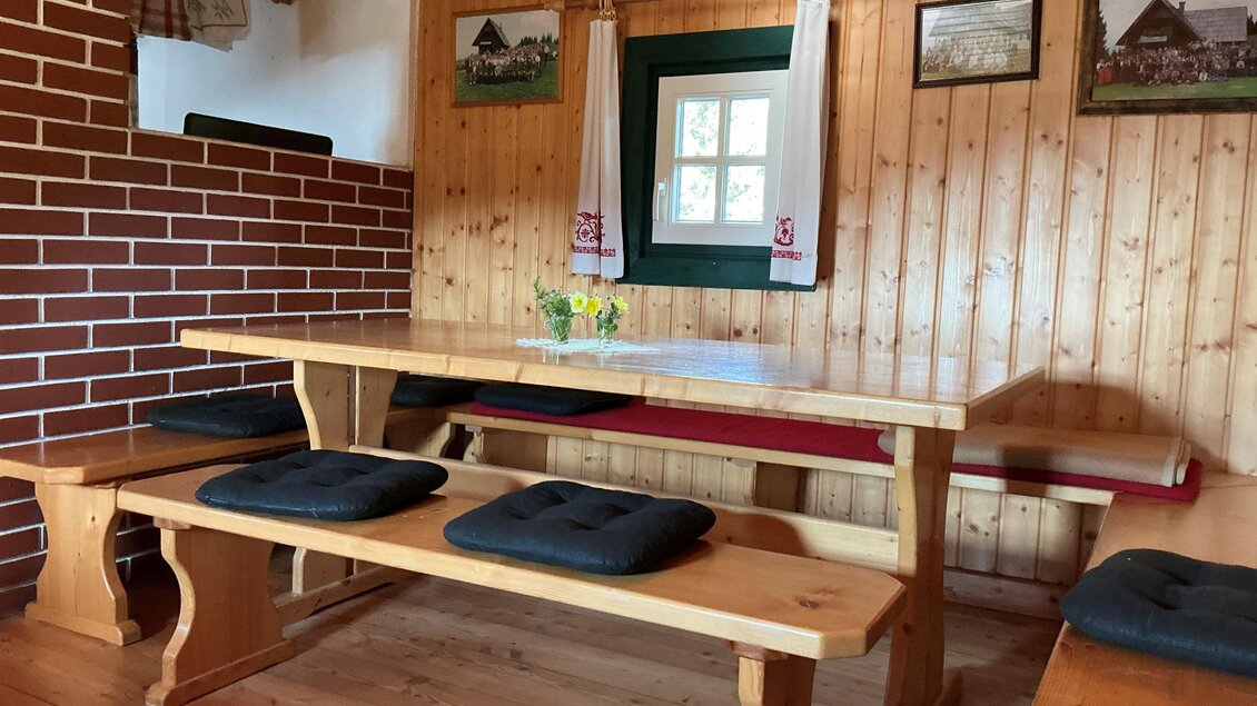 Ein gemütlicher Raum mit Holzwänden und einem großen Holztisch. Es gibt Bänke mit Kissen und einige dekorative Bilder an der Wand. | © Margareta Köstner