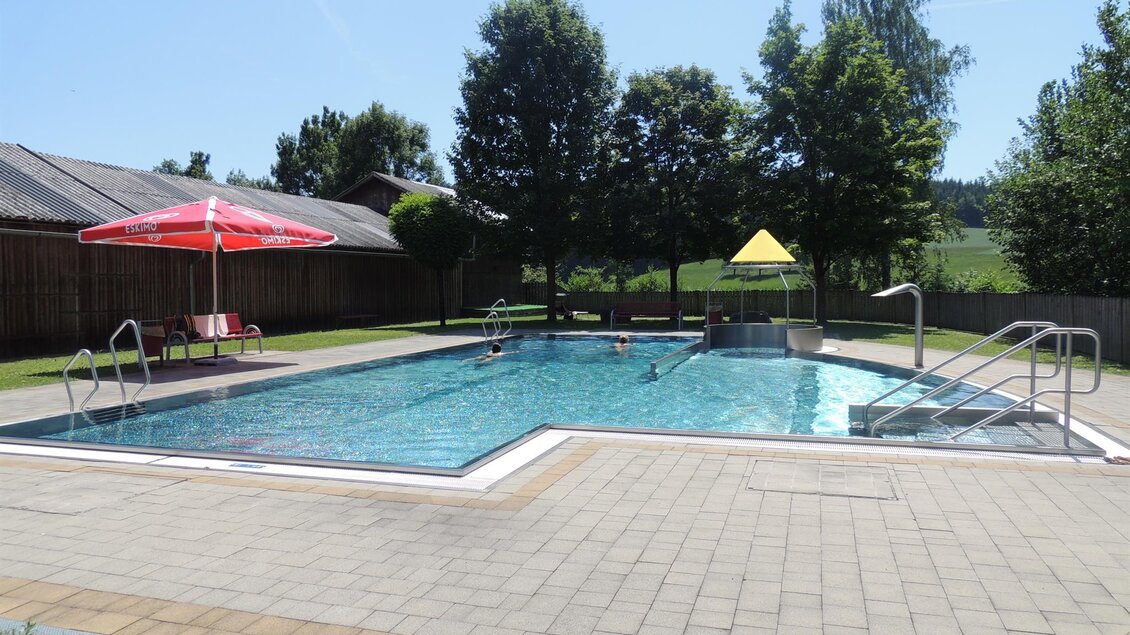 Ein schöner Schwimmbecken in einem ruhigen Außenbereich mit Sonnenschirmen und Bäumen. Der Himmel ist klar und die Umgebung ist einladend. | © WIP Erlebnisbad Wernersdorf