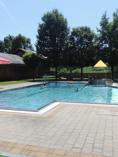 Ein schöner Schwimmbecken in einem ruhigen Außenbereich mit Sonnenschirmen und Bäumen. Der Himmel ist klar und die Umgebung ist einladend. | © WIP Erlebnisbad Wernersdorf