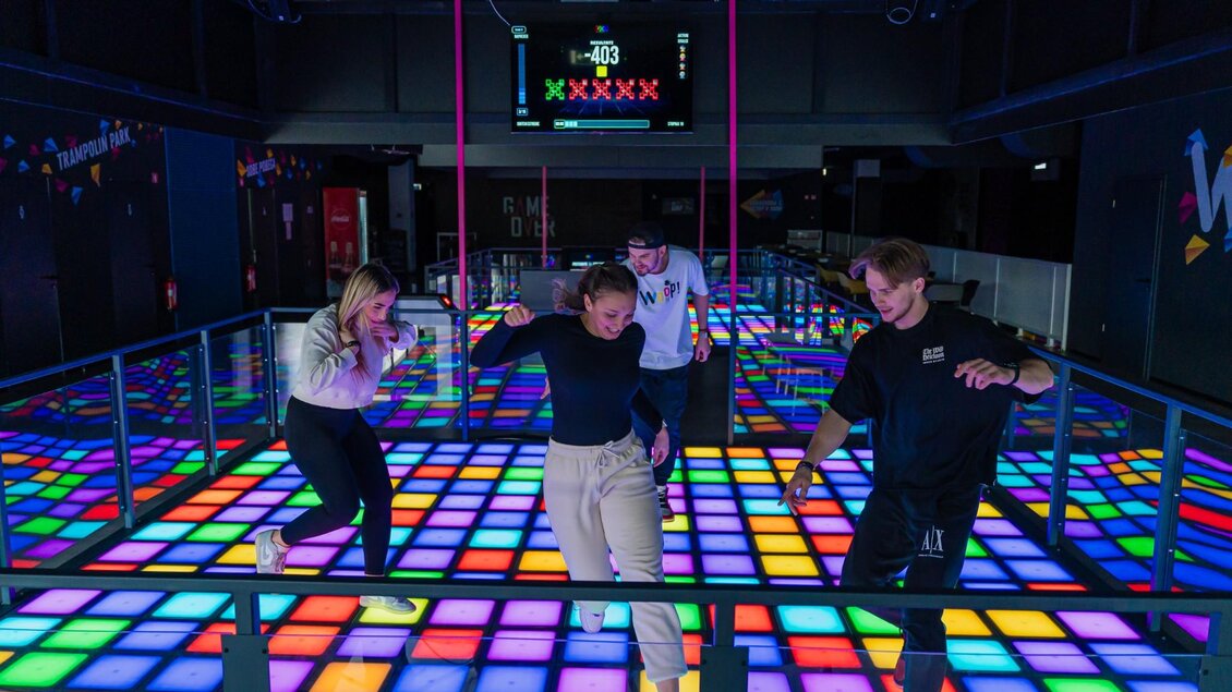 Vier junge Erwachsene bewegen sich auf leuchtendem LED-Boden in moderner Freizeithalle | © WOOP!