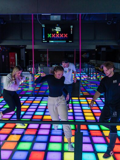 Vier junge Erwachsene bewegen sich auf leuchtendem LED-Boden in moderner Freizeithalle | © WOOP!