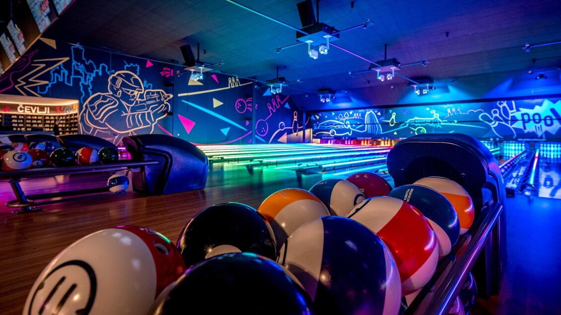 Bunte Bowlingkugeln vor beleuchteter Bahn mit Neonwand in moderner Indoorhalle | © WOOP!