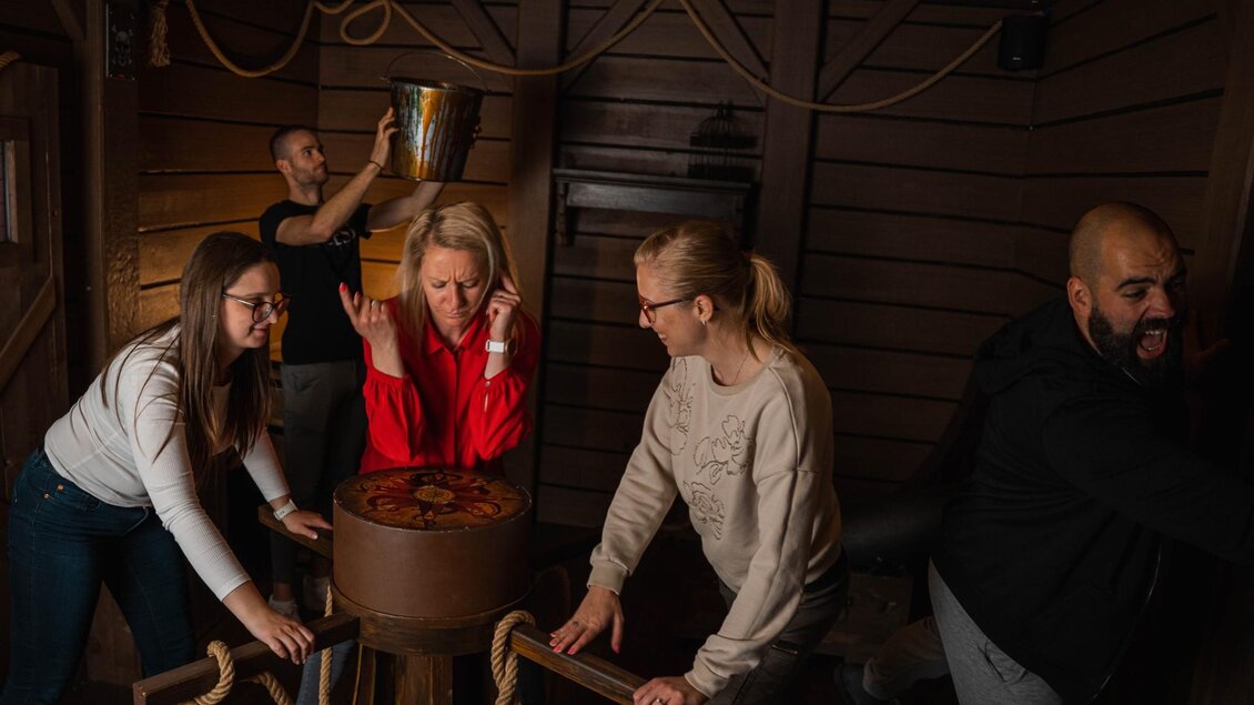 Fünf Erwachsene lösen gemeinsam ein Rätsel in einem thematisch gestalteten Piratenraum | © WOOP!