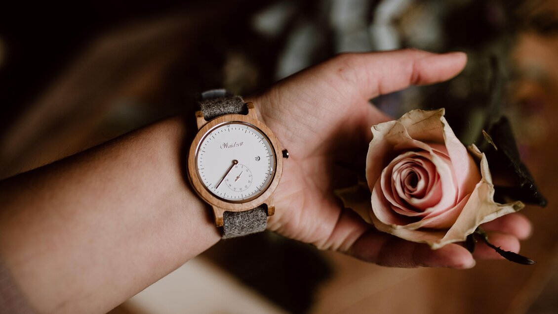 Eine Hand hält eine elegante Uhr und eine zarte Rose. Die Kombination aus Accessoire und Blume vermittelt einen romantischen und stilvollen Eindruck. | © Mira Schaffer