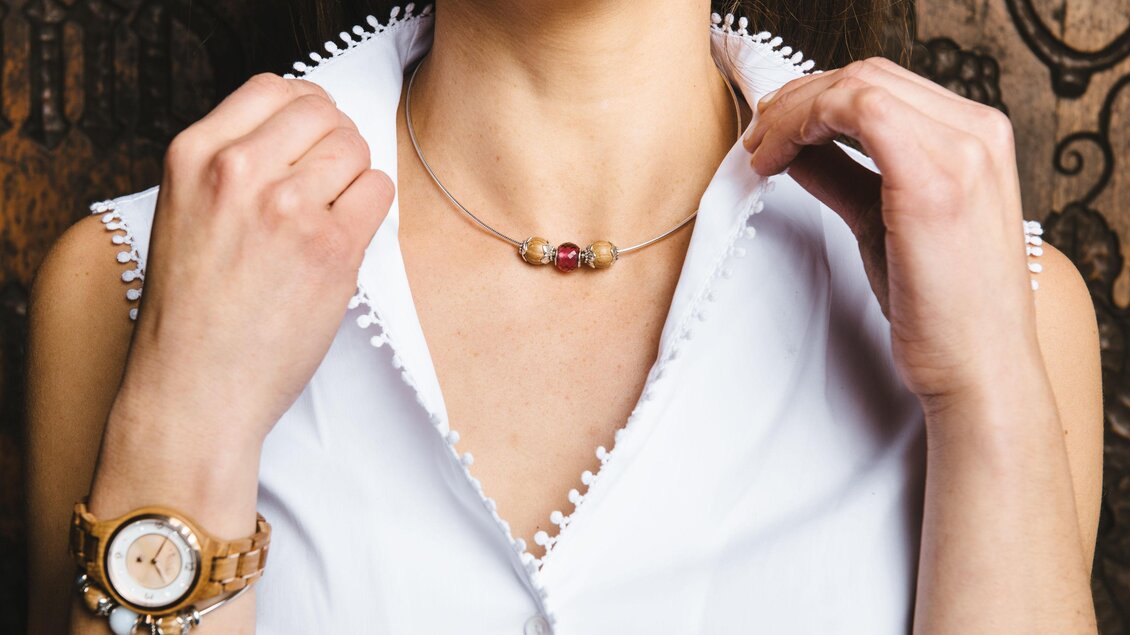 Eine Frau trägt eine elegante Halskette und eine modische Uhr. Sie hat die Knöpfe ihrer blauen Bluse geöffnet, was einen stilvollen Look betont. | © Lukas Bezila