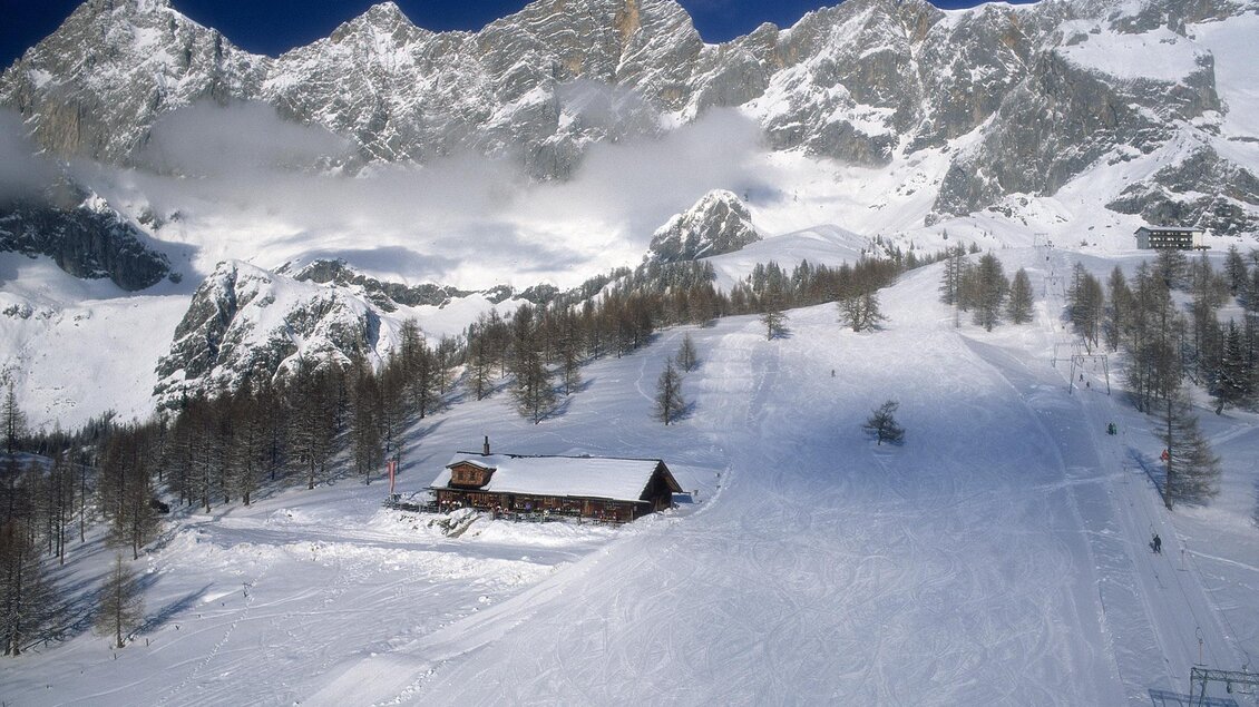 Eine schneebedeckte Landschaft mit majestätischen Bergen im Hintergrund. Im Vordergrund steht eine kleine Hütte, umgeben von einem Winterparadies. | © Raffalt