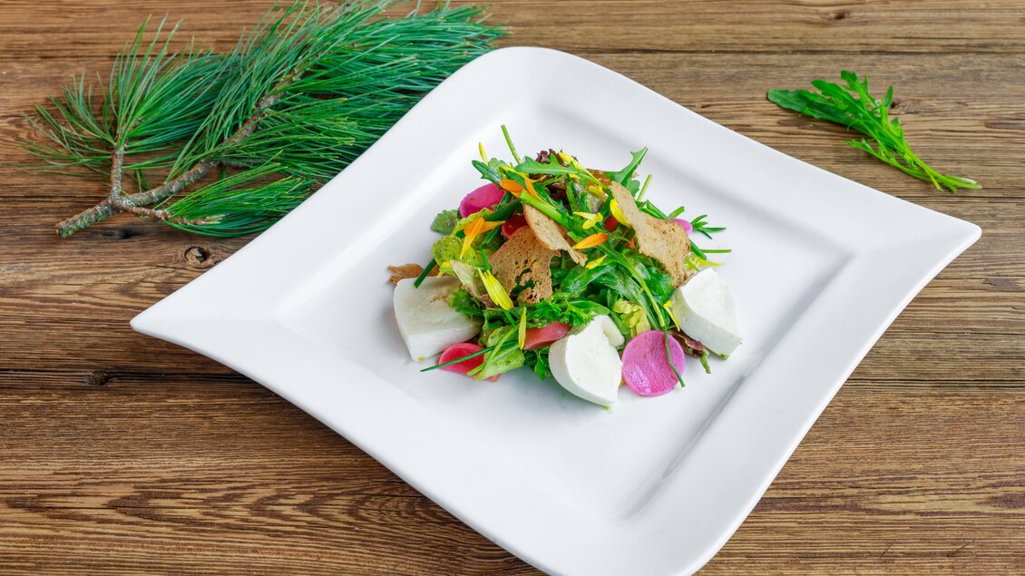 Ein frischer Salat mit buntem Gemüse, Kräutern und knusprigem Brot. Der Salat ist auf einem stilvollen weißen Teller angerichtet und eignet sich perfekt für eine gesunde Mahlzeit. | © Schladming Dachstein