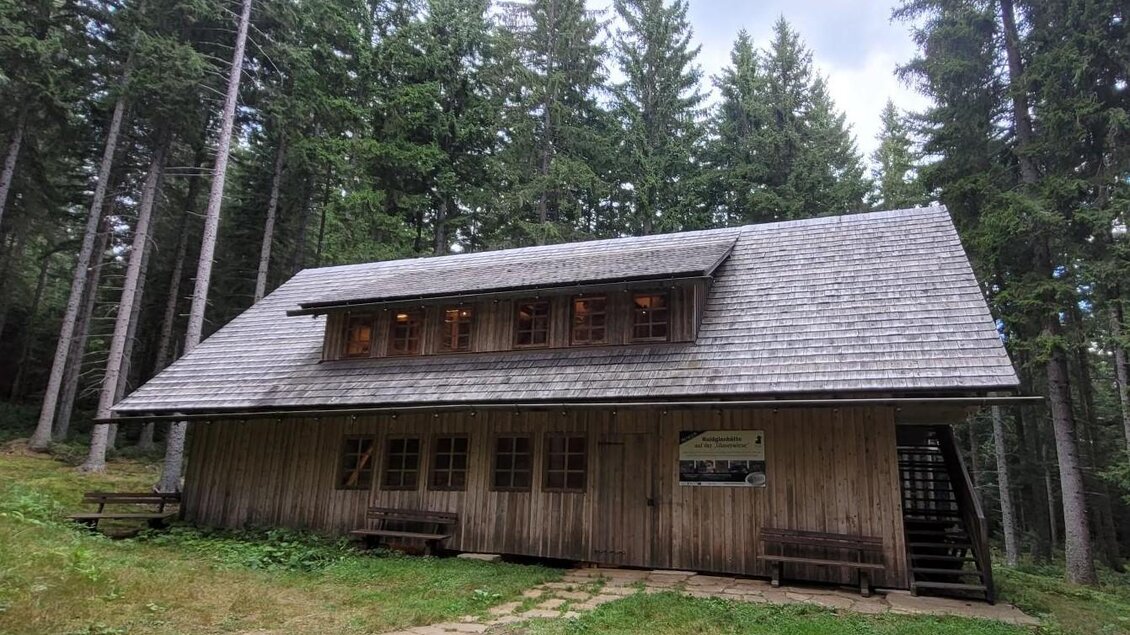 Ein Holzhaus in einem Waldgebiet, umgeben von hohen Bäumen. Der Himmel ist bewölkt und das Gelände ist grün und einladend. | © TV Südsteiermark - Irene Löschnig
