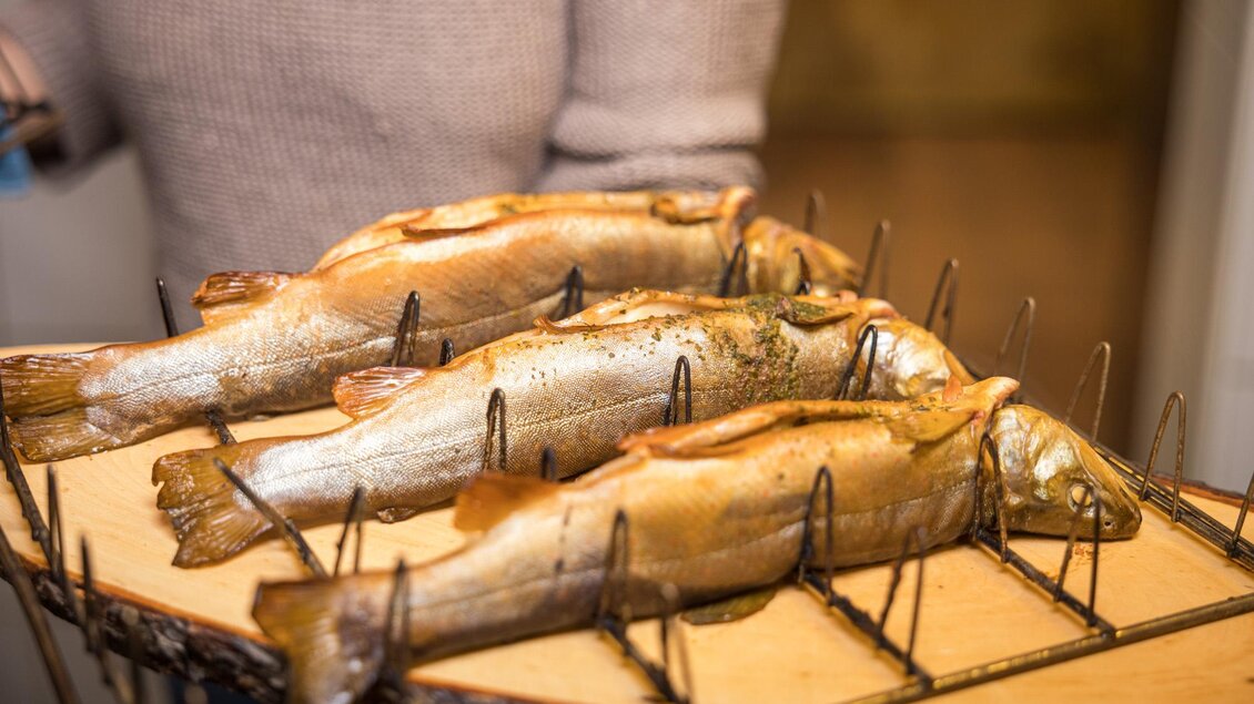 Drei gegrillte Fische auf einem Holzbrett. Sie sind auf einem speziellen Gestell platziert und wirken appetitlich. | © Netzwerk Kulinarik wildbild