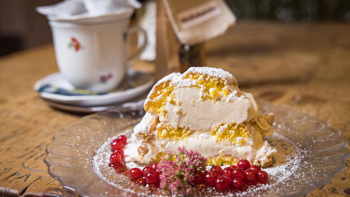 Ein köstliches Dessert mit Schichten aus Sahne und Früchten, garniert mit roten Johannisbeeren. Der Teller ist auf einem rustikalen Holztisch präsentiert. | © Netzwerk Kulinarik wildbild