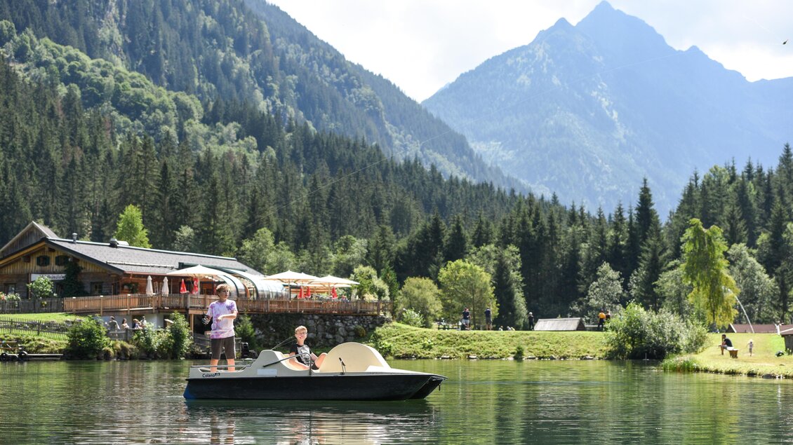 Ein schöner See umgeben von Bergen und Wäldern. Zwei Personen genießen eine Bootsfahrt in der Nähe eines gemütlichen Gasthauses. | © Waldhäuslalm/Shootingstar