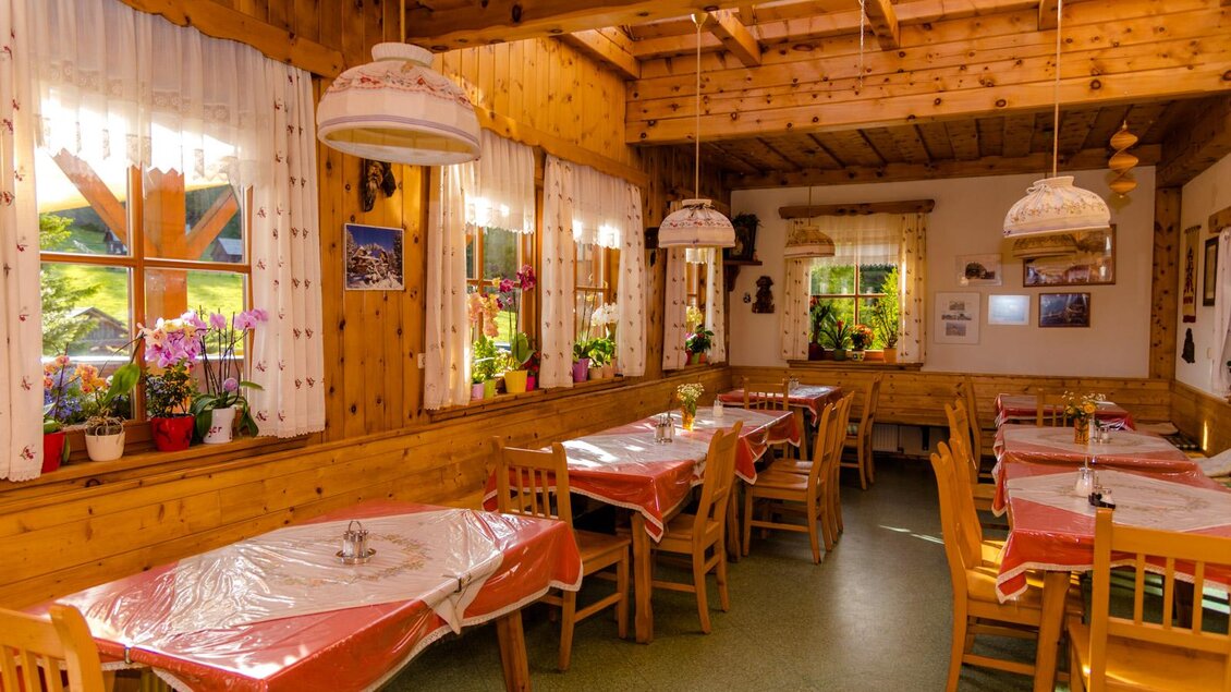 Ein gemütliches Restaurant mit Holzwänden und Tischen, die mit roten Tischdecken gedeckt sind. Viele Fenster lassen viel Licht hinein und Pflanzen schmücken den Raum. | © Waldheimhütte
