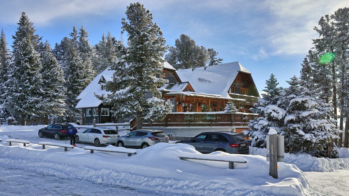 Ein schönes Haus im Winter, umgeben von schneebedeckten Bäumen. Autos stehen entlang der Straße auf frischem Schnee. | © Weges