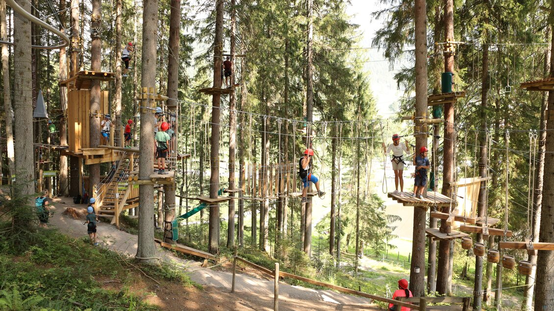Ein Hochseilgarten in einem Wald mit verschiedenen Kletterstationen. Menschen in bunten Helm klettern und genießen die Aktivitäten in der Natur. | © Hans-Peter Steiner