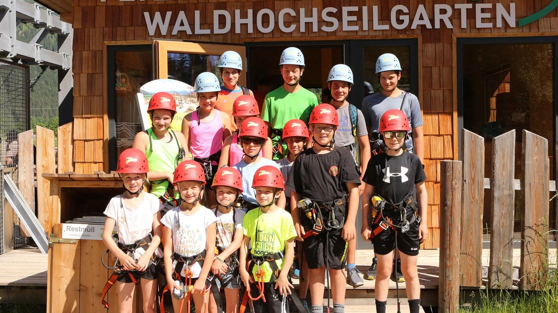 Eine Gruppe von Kindern und Jugendlichen steht vor dem Waldhochseilgarten mit Helmen und Kletterausrüstung. Sie lächeln und sind bereit für ein Abenteuer in der Natur. | © Erlebnis Rittisberg