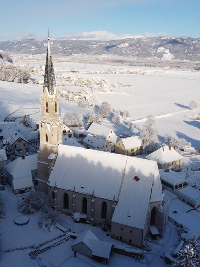 A snow-covered village with a church and surrounding houses. The landscape is calm and picturesque under the clear sky. | © Diazöse Graz Seckau