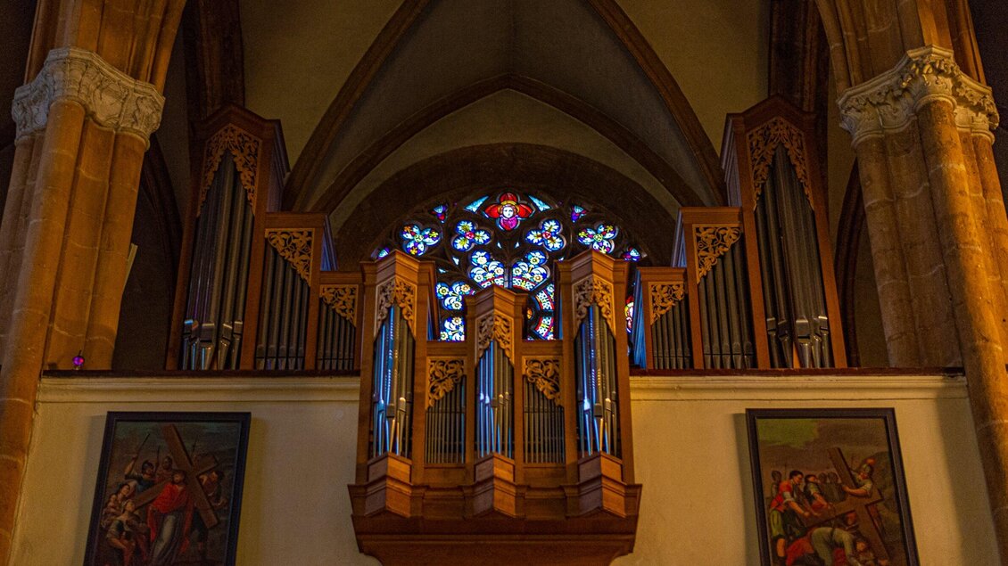 Eine Kirchenorgel steht im Hintergrund, umgeben von bunten Kirchenfenstern. An den Wänden hängen historische Gemälde. | © TV Region Graz - Mias Photoart