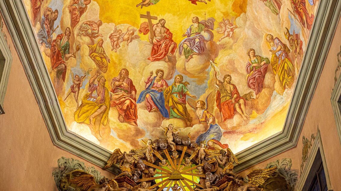 Eine kunstvoll bemalte Decke mit Szenen aus der religiösen Geschichte. Mehrere Figuren und Engel sind zwischen Wolken und goldenen Akzenten dargestellt. | © TV Region Graz - Mias Photoart