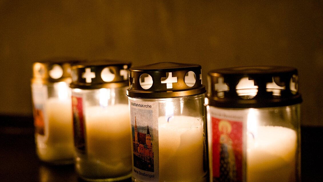 Vier Kerzen in Gläsern leuchten sanft im Dunkeln. Die Kerzen sind mit farbigen Bildern und dekorativen Löchern im Deckel verziert. | © TV Region OberGraz-Mias Photoart