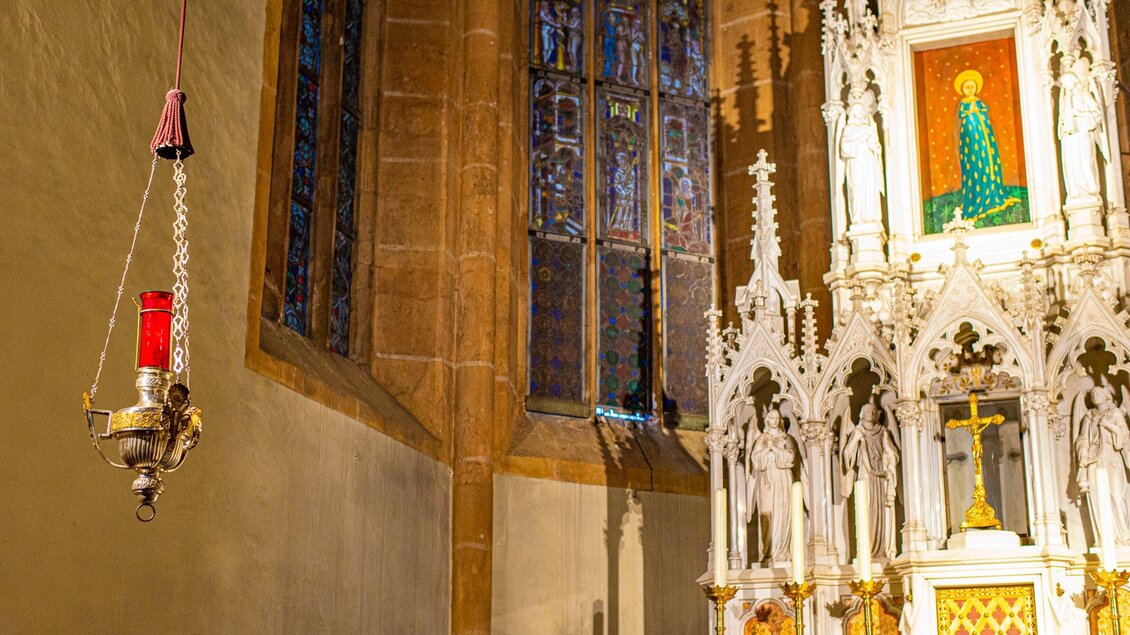 Ein schöner Kircheninnerer mit einem roten Licht und einem kunstvollen Altar. Die farbigen Fensterfenset und die Details des Altars verleihen dem Raum eine ruhige Atmosphäre. | © TV Region OberGraz-Mias Photoart