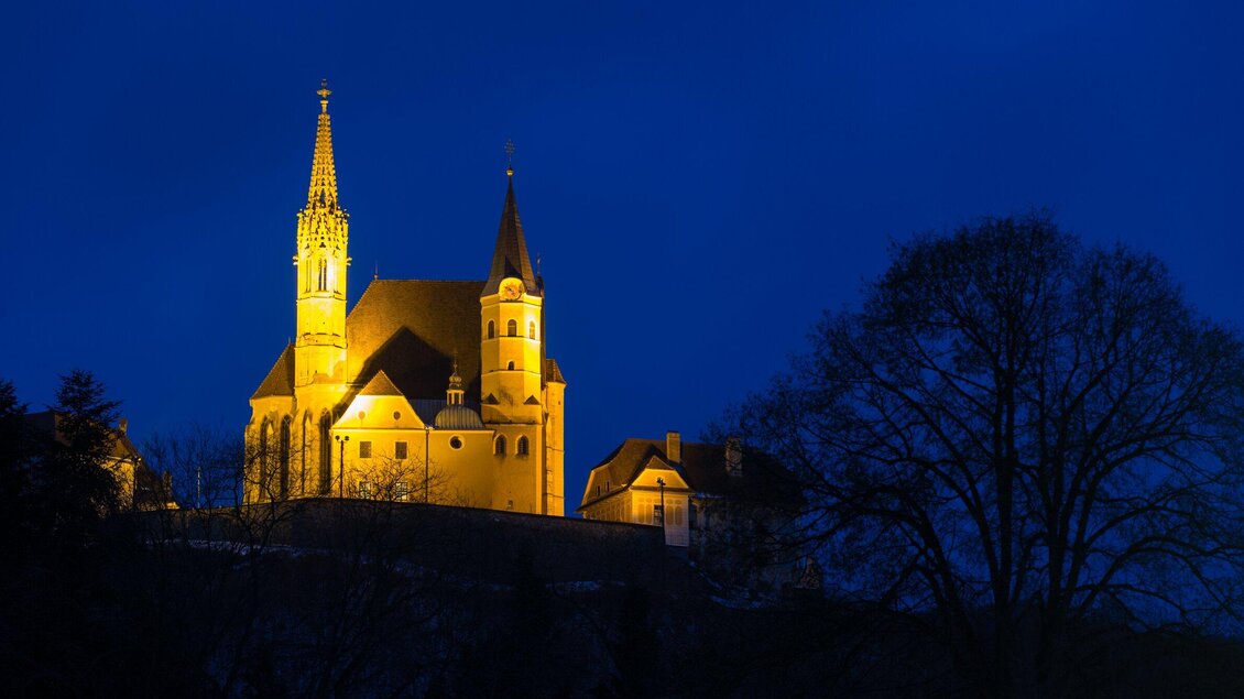 Eine beeindruckende Kirche bei Nacht, beleuchtet von warmem Licht. Der klare, blaue Himmel bildet einen schönen Kontrast zur Architektur. | © Region Graz - Harry Schiffer
