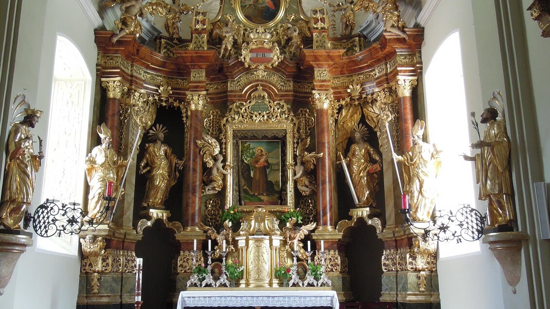 Eine prächtige Kirche mit einem reich verzierten Altar und kunstvollen Statuen. Der Innenraum ist hell erleuchtet und mit rotem Teppich ausgelegt. | © TV ERZBERG LEOBEN