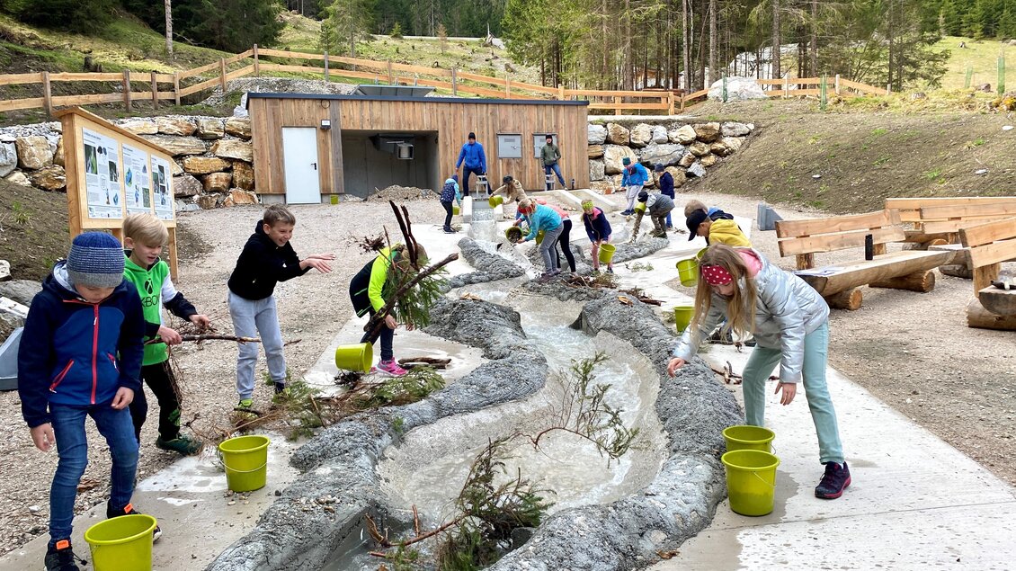 Kinder spielen im Freien und arbeiten an einem wasserspielplatz. Sie sammeln Zweige und andere Materialien in bunten Eimern. | © Martin Huber