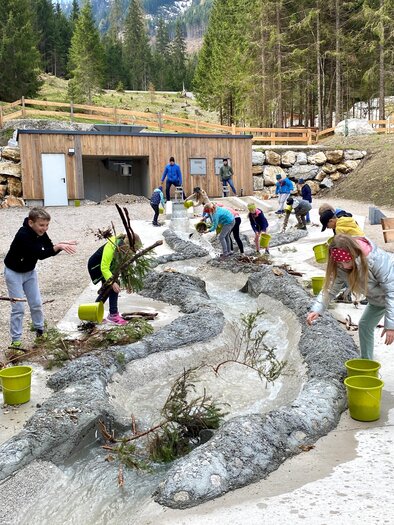 Children play outside and work at a splash pad. They collect twigs and other materials in colorful buckets. | © Martin Huber