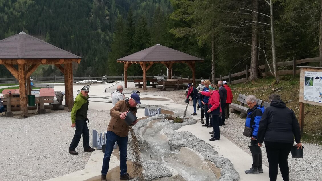 Eine Gruppe von Menschen erkundet einen naturbelassenen Wasserlauf in den Bergen. Im Hintergrund sind Pavillons und Bäume sichtbar. | © Wassererlebnis Öblarn