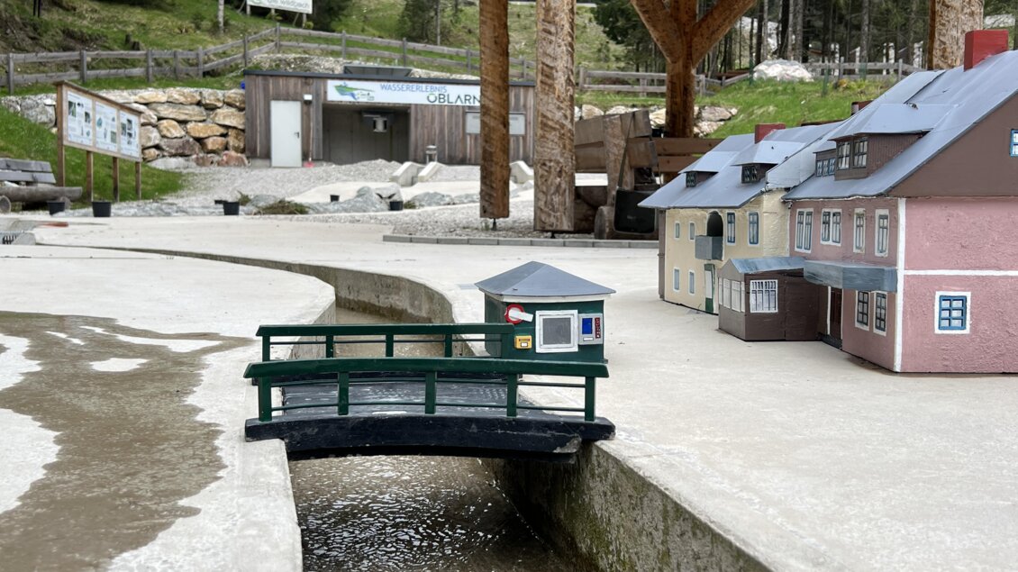 Eine Miniaturlandschaft mit einem kleinen Brückchen und Häusern. Im Hintergrund sieht man eine Holzstruktur und Bäume. | © Wassererlebnis Öblarn