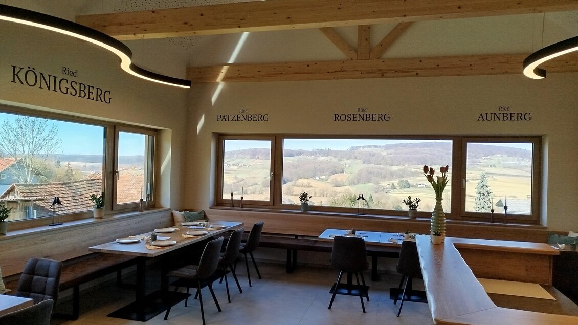 Ein heller Innenraum mit Holzbalken und Fensterblick auf die Landschaft. Die Möbel sind modern und einladend mit eleganten Tischen und Stühlen. | © Weingut Hopfer