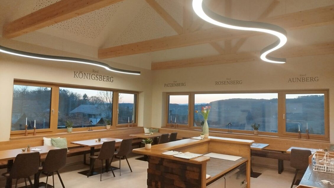 Moderne Innenansicht eines gemütlichen Raumes mit großen Fenstern und Holzdetails. Die Beleuchtung schafft eine einladende Atmosphäre und bietet einen Blick auf die Landschaft.