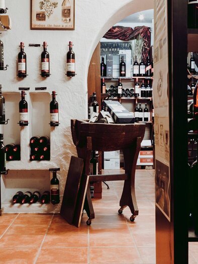 Ein gemütlicher Weinladen mit zahlreichen Regalen voller Weinflaschen. Im Hintergrund ist ein Holzregal und eine einladende Atmosphäre zu sehen. | © Snowcorn Laboratory