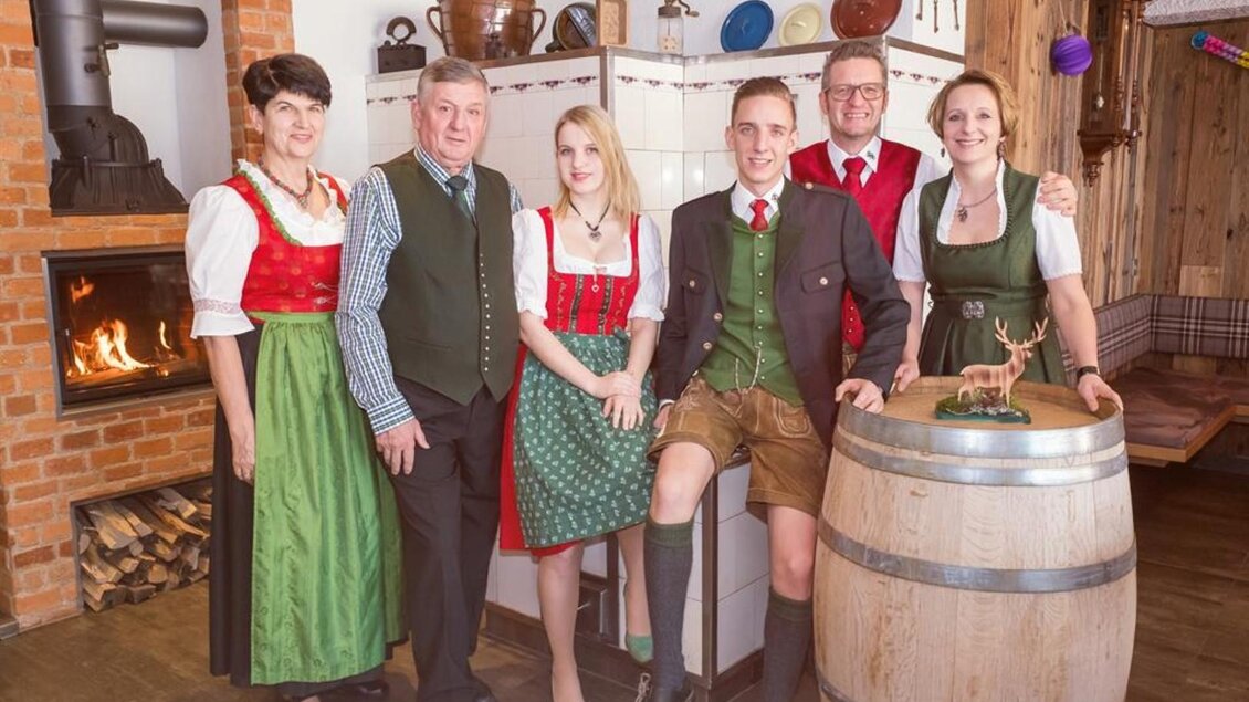 Eine Gruppe von Menschen in traditioneller bayerischer Tracht steht in einem gemütlichen Raum. Im Hintergrund ist ein Kamin zu sehen, und sie lächeln freundlich in die Kamera. | © Netwerker