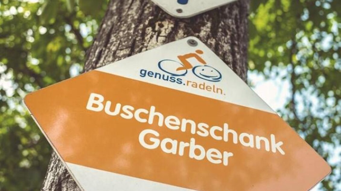 Ein Wegweiser an einem Baum zeigt die Route der "2-Flüsse Tour" und verweist auf den "Buschenschank Garber". Die Schilder sind bunt und informativ. | © Netwerker