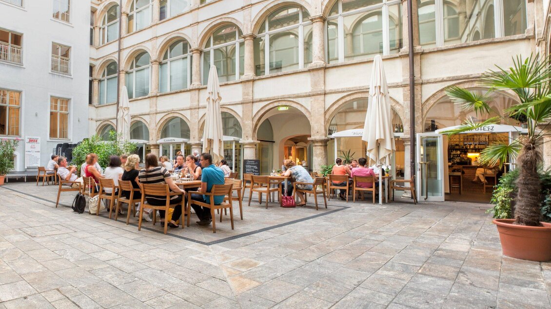 Ein gemütlicher Innenhof mit vielen Sitzplätzen. Gäste genießen das Essen unter Sonnenschirmen. | © Klapotetz